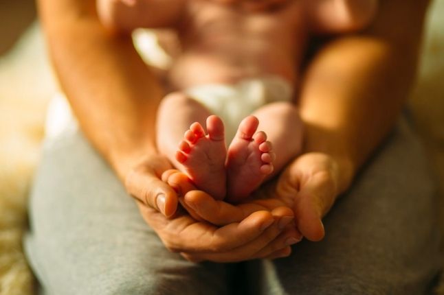 Vater haelt die Fueße eines Neugeborenen, was Sicherheit und Geborgenheit symbolisieren soll